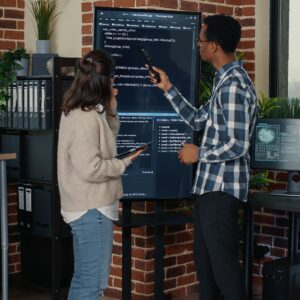 Team of database admins analyzing source code on wall screen tv comparing errors using tablet
